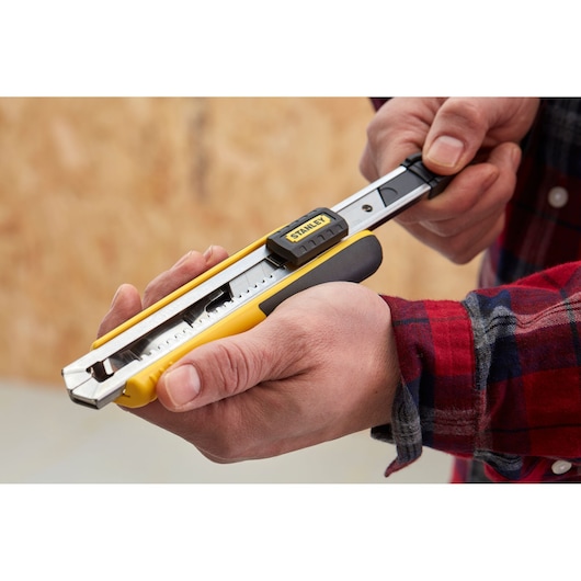Stanley 0-10-481 utility knife with yellow and black handle in hand, close-up side view.