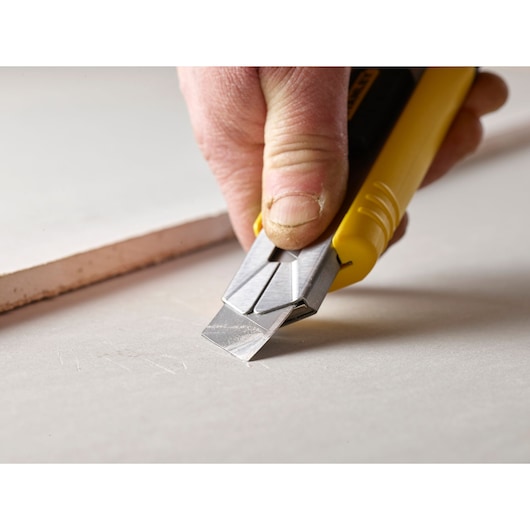 Photo of STANLEY 0-11-725 utility knife cutting drywall, close-up of the blade and yellow handle.