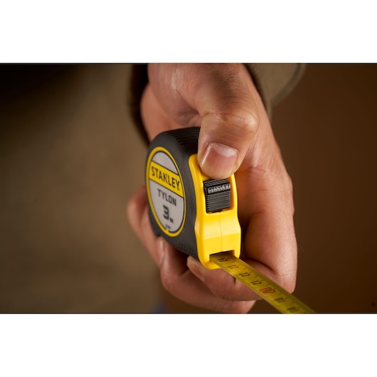 Photo of STANLEY 0-30-687 tape measure being held, yellow and black, with extended measuring blade.