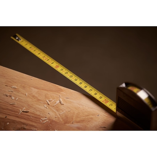 STANLEY 0-32-125 tape measure extended on wooden surface, yellow blade, side angle photography.