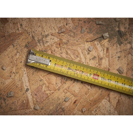 STANLEY 0-33-442 tape measure close-up on plywood surface with small stones, showing measurement markings.