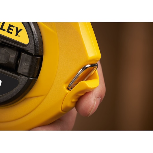 STANLEY 0-34-108 tape measure close-up showing yellow case, metal hook, and part of hand holding it.