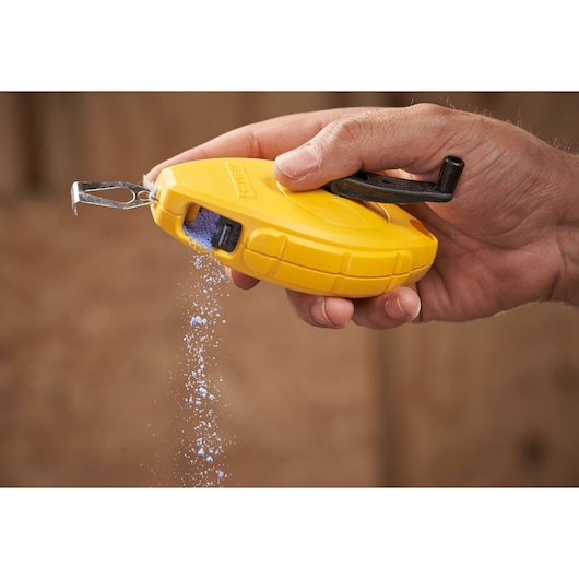 STANLEY 0-47-440 chalk line reel in yellow, hand-held with blue chalk pouring out, close-up photography.