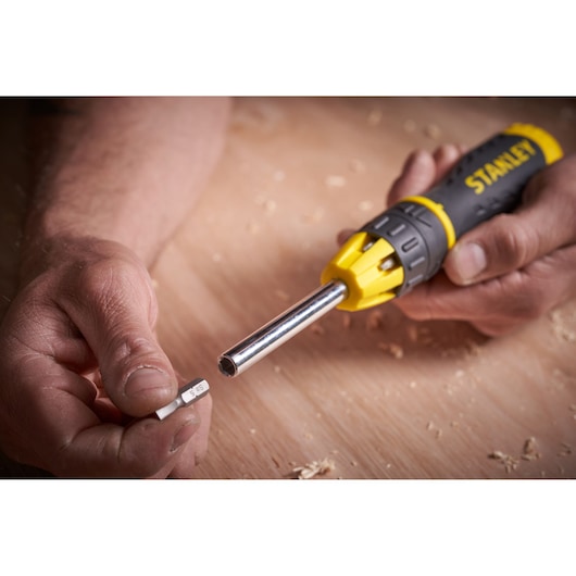 Photo of STANLEY 0-68-010 screwdriver with yellow and black handle, person inserting bit, close-up view.
