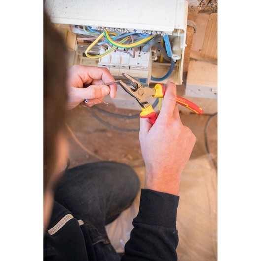 Photo of STANLEY 0-84-001 pliers being used to cut wire during electrical work near a fuse box.