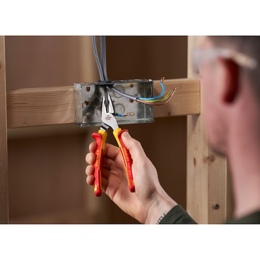 Photo of STANLEY 0-84-001 insulated combination pliers being used to grip electrical wires in a metal junction box.