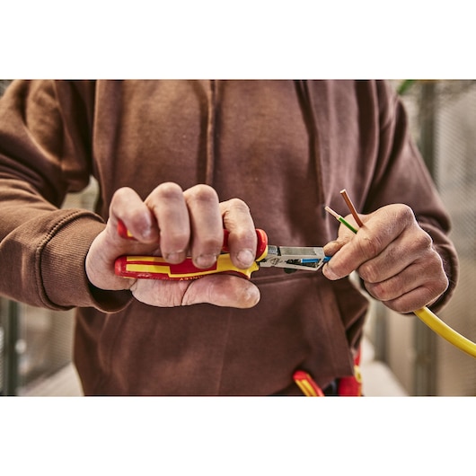 Photo of a person using STANLEY 0-84-010 insulated pliers to strip electrical wire.