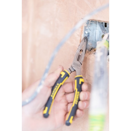 STANLEY 0-89-872 long nose pliers with black and yellow handles used for wiring in construction wall.