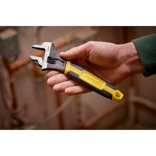 STANLEY 0-90-947 adjustable wrench with yellow and black ControlGrip handle, shown in hand indoors.