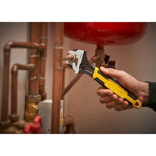 STANLEY 0-90-949 adjustable wrench with yellow-black handle tightening a copper pipe in plumbing.