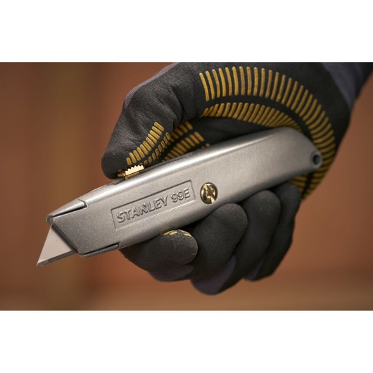 STANLEY 1-10-099 utility knife held in gloved hand, close-up side view, silver metal body.