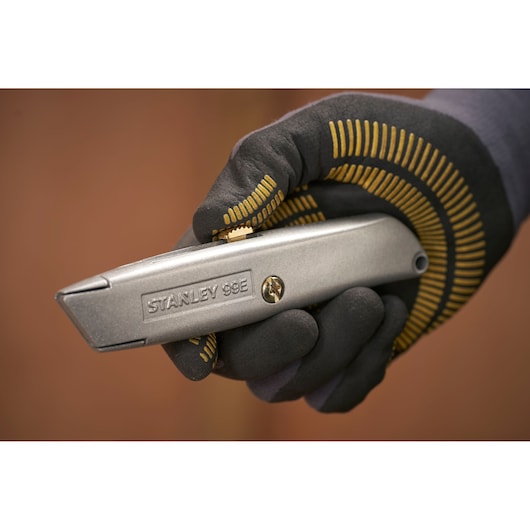 Photo of STANLEY 1-10-099 utility knife held in gloved hand, silver metal body, close-up view.