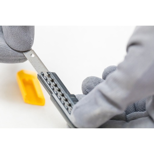STANLEY 1-10-150 utility knife blade held by gloved hand, yellow blade holder visible on white background.