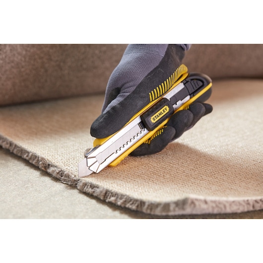 STANLEY 1-10-481 utility knife cutting carpet, close-up, held by gloved hand.