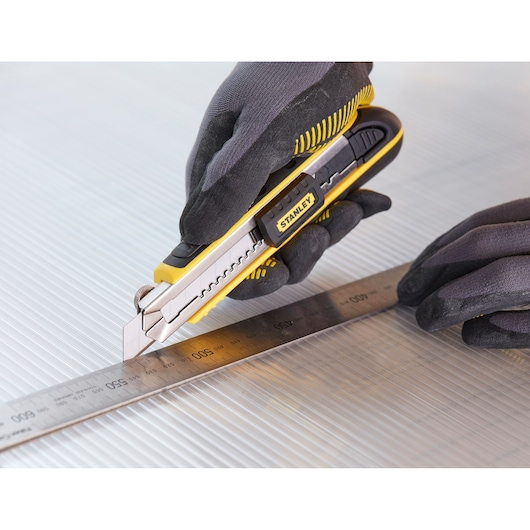 STANLEY 1-10-481 utility knife held by gloved hands cutting along a metal ruler on corrugated surface.