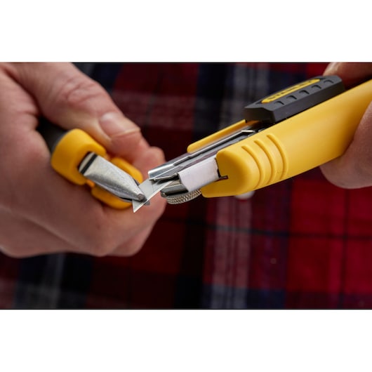 Close-up of STANLEY 1-10-481 yellow utility knife, person snapping off blade segment.