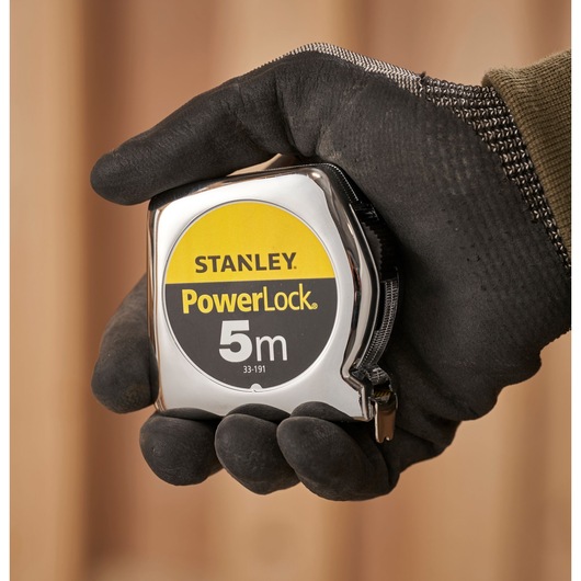 STANLEY 1-33-191 tape measure PowerLock 5m held in a gloved hand, close-up photography.