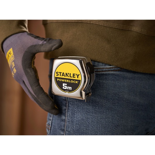STANLEY 1-33-195 tape measure clipped to jeans belt, photographed close-up with worker glove visible.