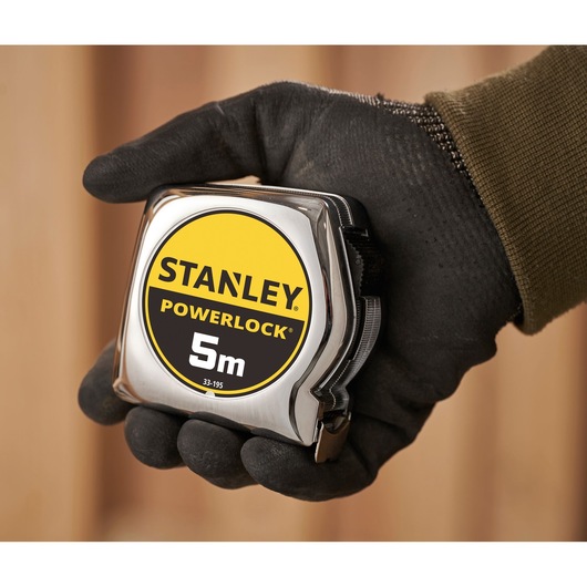 STANLEY 1-33-195 PowerLock 5m tape measure with chrome case held in gloved hand, close-up.