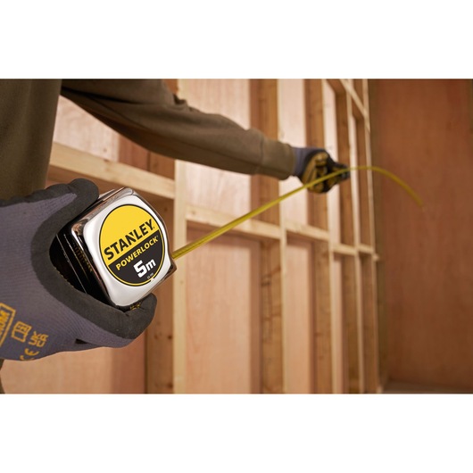 Stanley 1-33-195 PowerLock 5m tape measure in use against wooden wall frame, close-up angle.