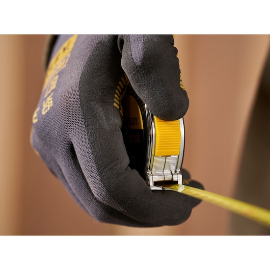Photo of a gloved hand holding a STANLEY 1-33-238 tape measure, yellow and black, product in use.