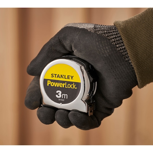 Photo of STANLEY 1-33-522 PowerLock 3m tape measure in gloved hand, foreground close-up.