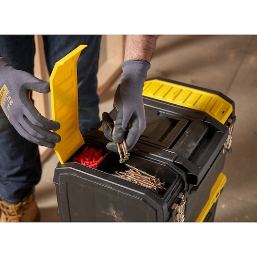 STANLEY 1-70-326 tool box close-up with yellow compartment open, screws and wall plugs visible, gloved hands holding screws.