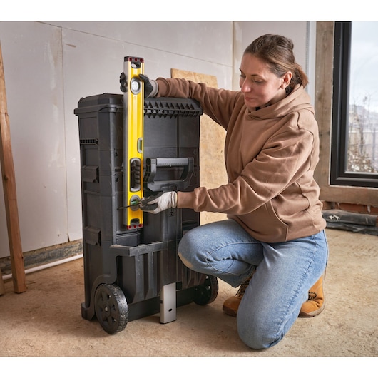 STANLEY 1-79-206 tool trolley with wheels, side view, person using yellow level, indoor workshop.