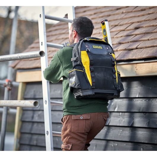 STANLEY 1-95-611 tool backpack in black and yellow shown on a person climbing a ladder outdoors.