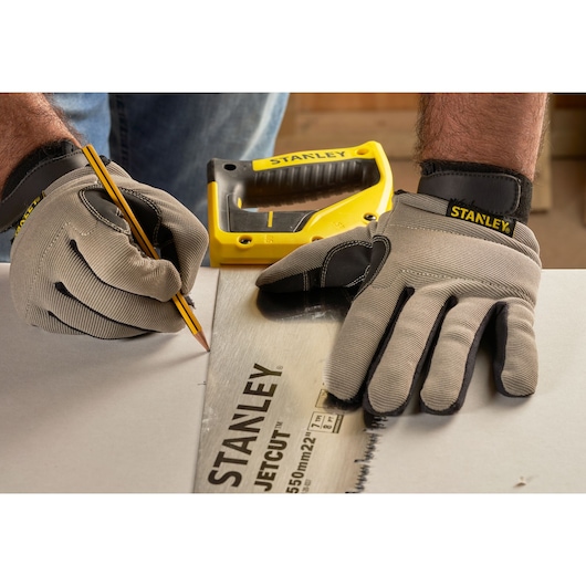 Stanley 2-20-037 JetCut handsaw on table, close-up angle, worker with gloves marking cut line.