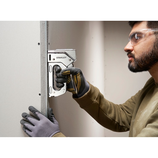 Stanley 6-TR110 heavy-duty staple gun used on drywall, close-up of gloved hands during construction task.