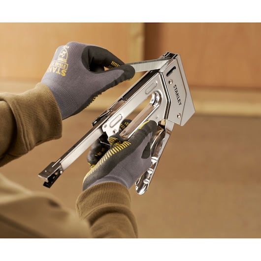 Stanley 6-TR110 staple gun held by gloved hands, inserting staples, close-up view.