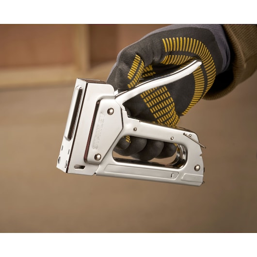 Photo of STANLEY 6-TR45 metal staple gun held by a gloved hand, close-up side view.