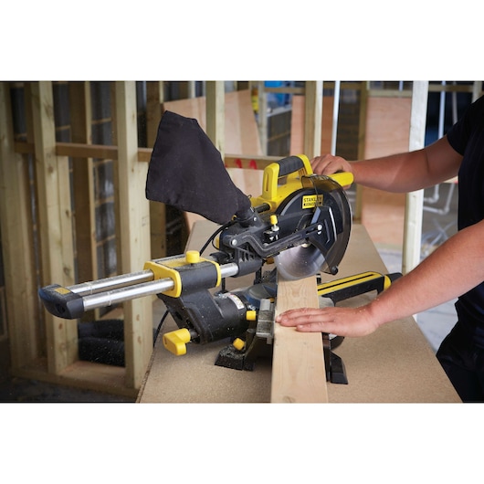 STANLEY FME721 sliding miter saw cutting wood in workshop, close-up side view showing hands guiding wood.