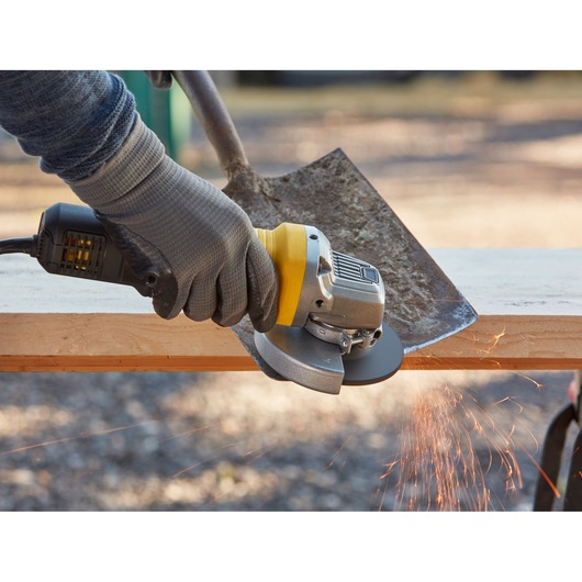 STANLEY FMEG210 angle grinder tool grinding a shovel blade, side view, with visible sparks.