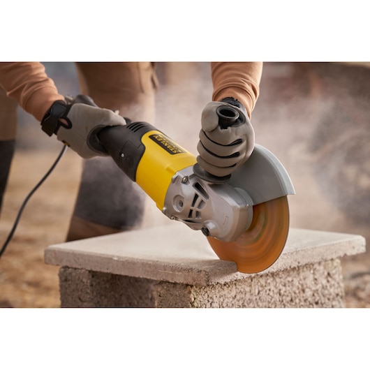 STANLEY FMEG232 angle grinder in use cutting concrete block, close-up view.