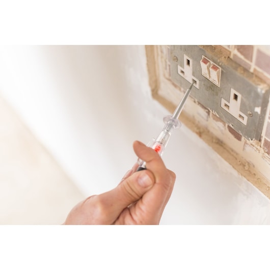 Photo of STANLEY FMHT0-64985 voltage tester used at electrical outlet, close-up hand view.