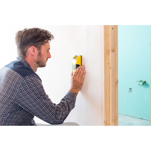 Photo of a person using a STANLEY FMHT0-77407 wall scanner tool against a white wall, product in hand.