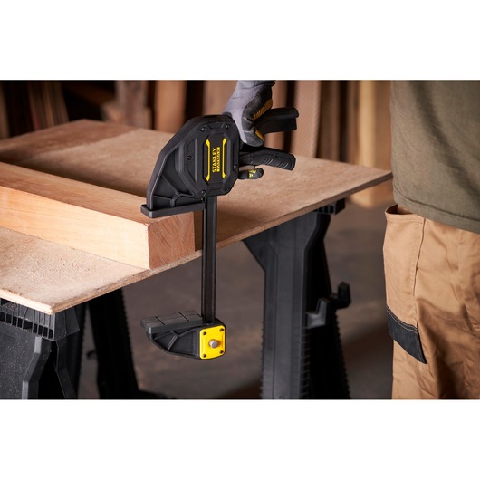 Stanley FMHT0-83238 trigger clamp securing wood on workbench, side angle view.