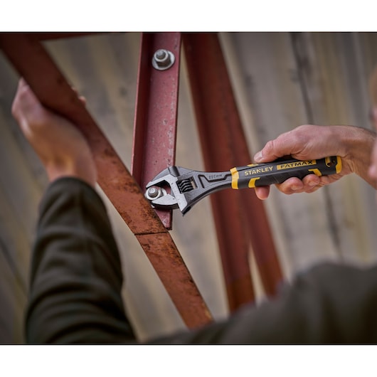 STANLEY FMHT13128-0 adjustable wrench, FATMAX series, used on a metal bolt, close-up photography.