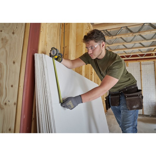 STANLEY FMHT38214-0 tape measure in use measuring drywall panel, construction setting.