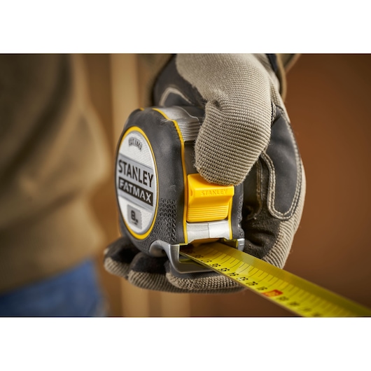STANLEY FMHT38217-0 tape measure held in gloved hand, close-up angle, yellow and black casing.