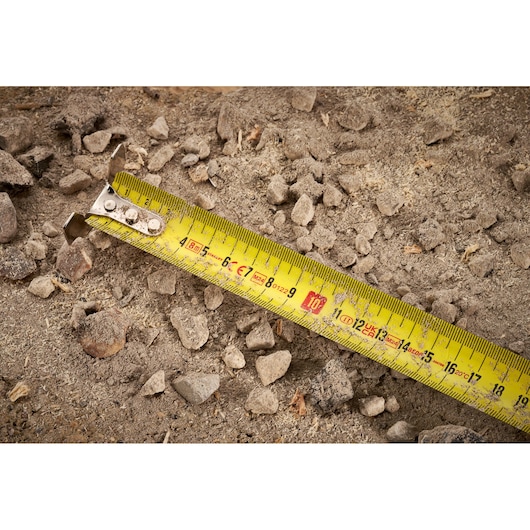 STANLEY FMHT38217-0 yellow tape measure photography showing close view on rocky soil.