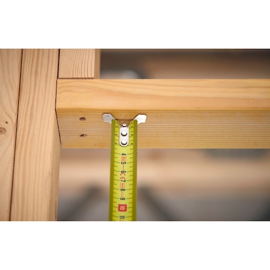 STANLEY FMHT38217-0 tape measure in use measuring wooden frame, close-up front angle.