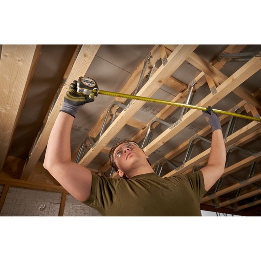 Photo of a worker measuring ceiling joists with a STANLEY FMHT38232-0 tape measure in a construction area.