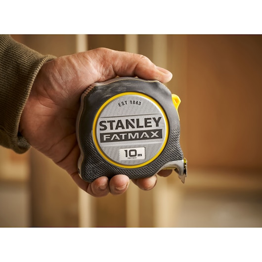STANLEY FMHT38232-0 tape measure FATMAX 10m held in hand, black and yellow housing.