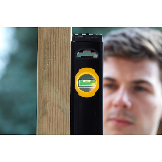STANLEY FMHT42447-1 spirit level with yellow vial, shown vertically against wooden beam, close-up.