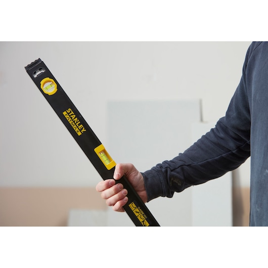 Photo of a person holding a STANLEY FATMAX level, SKU FMHT42554-1, black and yellow, used in construction.