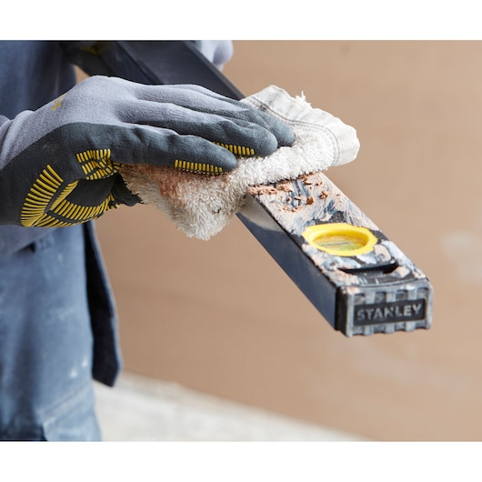 Photo of STANLEY FMHT42562-1 level being cleaned with a cloth by a gloved hand, construction context.