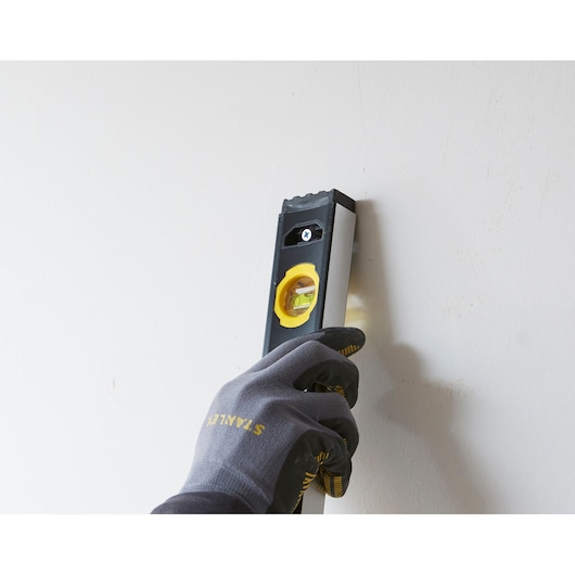Photo of STANLEY FMHT42562-1 spirit level held vertically against a wall by a gloved hand.